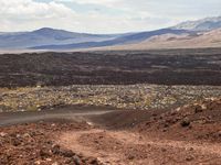 a dirt road that is winding through the barren area of land below mountain ranges and large rocks