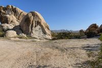 rock formations are dotted with sand and bushes in a desert area under a blue sky