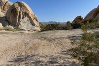 rock formations are dotted with sand and bushes in a desert area under a blue sky