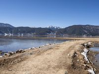 a dirt road beside some water and mountains with a sky background, with no clouds