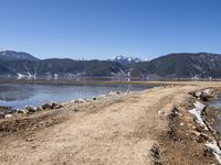 a dirt road beside some water and mountains with a sky background, with no clouds