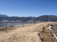 a dirt road beside some water and mountains with a sky background, with no clouds