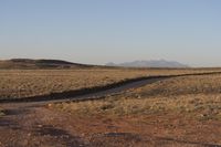 the dirt road through the country leads towards mountains and a stream of water in a barren landscape