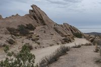 a dirt road and some rocks in the desert on a cloudy day and there is a person on a motorcycle