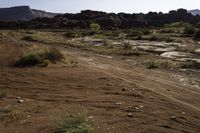 a dirt road through a desert field next to a mountain range and mountains in the background