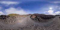 panoramic image of a dirt road in a desert landscape with mountains and clouds