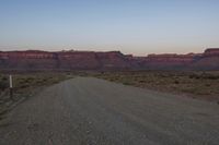 the dirt road leads through the desert to mountains at dusk - - - - -