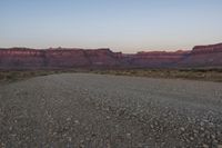 the dirt road leads through the desert to mountains at dusk - - - - -