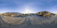 the view from a spherical lens of a dirt road in the desert with mountains in the background