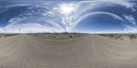 a panoramic shot looking over an open dirt road in the desert with a bright sky