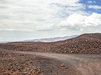 a dirt road with a white motorcycle going around it on a dry landscape with mountains in the distance