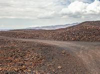 a dirt road with a white motorcycle going around it on a dry landscape with mountains in the distance