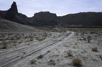 a dirt road is shown in front of an eroded mountain slope with the trail in the middle