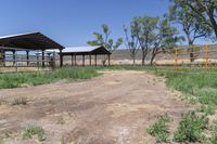 a dirt road with some green trees and bushes in the background that are fenced off by a gate