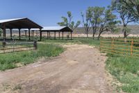 a dirt road with some green trees and bushes in the background that are fenced off by a gate