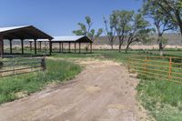 a dirt road with some green trees and bushes in the background that are fenced off by a gate