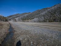 a dirt road with hills in the background and two people casting shadows on it on a sunny day