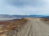 a dirt road with mountain in the background and mountains in the distance under cloudy skies