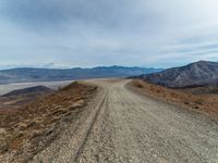 a dirt road with mountain in the background and mountains in the distance under cloudy skies