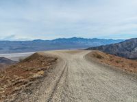 a dirt road with mountain in the background and mountains in the distance under cloudy skies