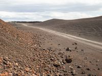 a dirt road with some rocks and gravel near the road that passes by on a cloudy day