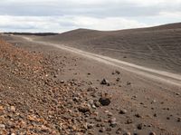 a dirt road with some rocks and gravel near the road that passes by on a cloudy day