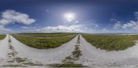 a road going down a dirt road near a field with clouds in the background and sun