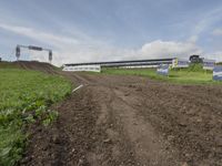 a dirt road leading to a track with a large building on the hill in the background