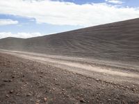 a white motorcycle is parked along the side of a dirt road in front of a hill