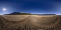 a view of a dirt road in a barren area near the mountains, with the sun in the sky