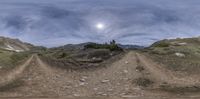 a wide angle panoramic view of a dirt road near a mountain with a sky background