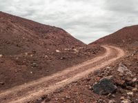 an image of a dirt road going up the mountain side with a couple rocks and large boulders on it