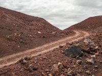 an image of a dirt road going up the mountain side with a couple rocks and large boulders on it