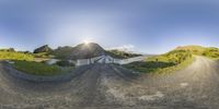 a dirt road near a mountain on a sunny day in front of a hill of grass and water