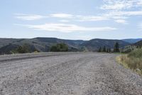 a dirt road in the middle of mountains with hills and trees in the background of the photo