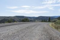 a dirt road in the middle of mountains with hills and trees in the background of the photo