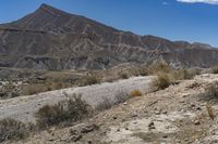 there is a dirt road with hills behind it in the desert of a mountain range