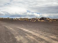 the dirt road runs alongside a large pile of rocks and boulders in the distance, with a few clouds visible