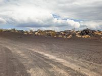 the dirt road runs alongside a large pile of rocks and boulders in the distance, with a few clouds visible