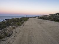 a dirt road leading towards a ocean by the shoreline at sunset in california on a hazy day