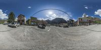 a 360 - view lens image of a dirt road in front of several buildings with a large archway at the end