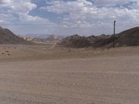 a dirt road winding through a large desert area near mountains and telephone lines and telephone lines