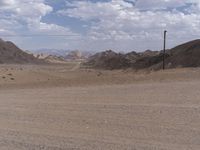 a dirt road winding through a large desert area near mountains and telephone lines and telephone lines