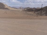 a dirt road winding through a large desert area near mountains and telephone lines and telephone lines