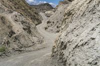 the dirt road through the mountains is rocky and narrow, with some clouds in the sky