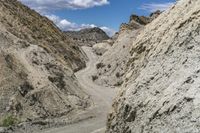 the dirt road through the mountains is rocky and narrow, with some clouds in the sky