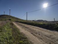 dirt road near a fence with wind turbines in the distance with blue skies and sun