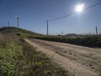 dirt road near a fence with wind turbines in the distance with blue skies and sun