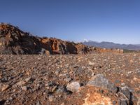 a dirt road next to the mountains with many rocks on it and a bench in front