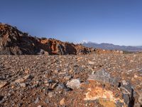 a dirt road next to the mountains with many rocks on it and a bench in front